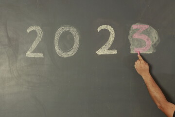 Mano de hombre escribiendo con gis 2023 en una pared gris con motivo del a&ntilde;o nuevo