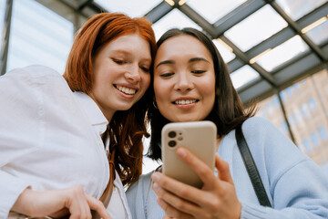 Young multinational women smiling and using cellphone indoors