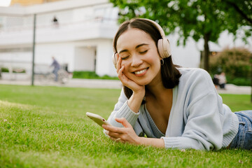 Young asian woman smiling and using cellphone while resting in park