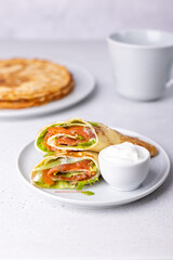 Pancakes with salmon (trout), sour cream and greenstuff. Thin, not sweet blinchiki stuffed with red fish. Traditional Russian and Ukrainian dish. Feast of Maslenitsa. Selective focus, close-up.