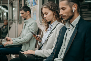passengers with smartphones sitting in a subway car .
