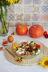 Aesthetic colorful vegetarian salad with edible flowers, peach, figs, basil and feta on ceramic...