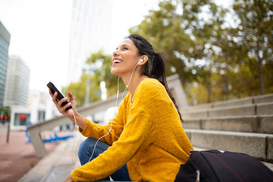 Side of young woman listening to music with earphones and cellphone in city