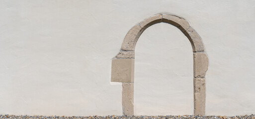 Panorama einer weiß verputzten alten Wand mit einem eingearbeiteten steinernen Torbogen