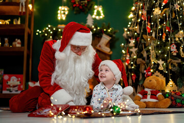 Nice boy having fun with Santa Clause while lying on the floor near Christmas tree. New Year concept