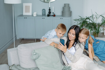 Obraz na płótnie Canvas mom with two kids watching videos on her smartphone.