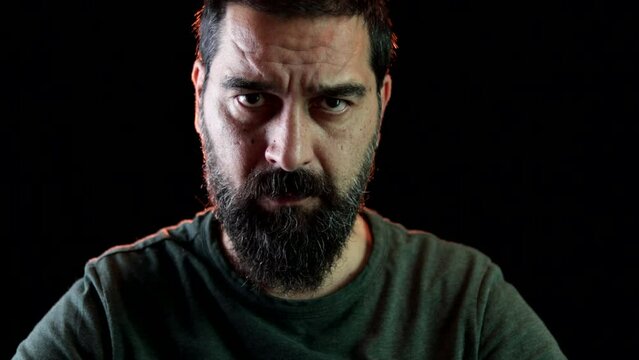 Portrait of bearded man sitting with serious face looking at the camera for a few seconds and then turning his head and looking away.