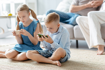 brother and sister with smartphones sitting on the floor in the living room.