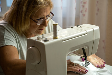 Woman seamstress with glasses concentrating while sewing at the sewing machine