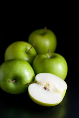 Green apples, whole, and halves isolated on a black background.
