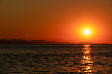 Fototapeta premium Panoramic view of sunset over Aegean Mediterranean Sea seen from Karydi beach, peninsula Sithonia, Chalkidiki (Halkidiki), Greece, Europe. Romantic atmosphere, reflection of the sunbeams on surface