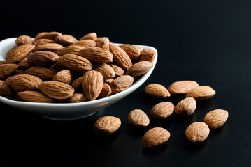 Almonds in a white ceramic bowl and placed on a black floor.