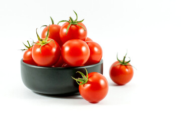 Red tomatoes in a black ceramic cup and placed on a white floor.