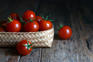 Fototapeta na wymiar Several red tomatoes are placed in a wicker container and put on a rustic wooden floor.