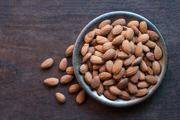 Almonds in a ceramic plate on a dark wooden floor, flat lay.