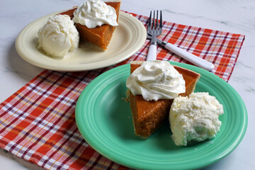 Two servings of pumpkin pie with a dollop of whipped cream and a scoop of vanilla ice cream.