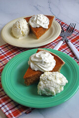 Two servings of pumpkin pie with a dollop of whipped cream and a scoop of vanilla ice cream.