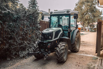 Modern green good-looking tractor stands in outside garage near agricultural fixtures and transport...