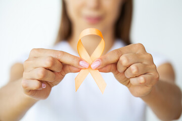 Woman in white t-shirt holding and showing orange awareness ribbon in her hands