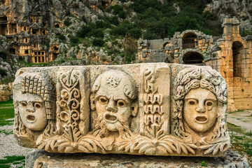 Preserved bas reliefs with floral ornaments and masks. Myra Ancient City rock tombs in background. Demre, Antalya, Turkey