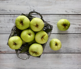 Basket of green apples, scattered apples on a light wooden background, top view. 