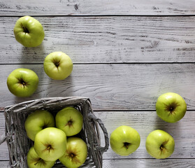 Basket of green apples, scattered apples on light wooden background, top view, flat lay. 