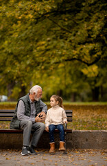 Grandfather spending time with his granddaughter on bench in park on autumn day
