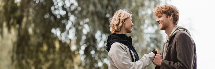 redhead man and blonde woman in coat smiling while holding hands outdoors, banner.