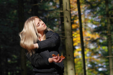 Dziewczyna trzymające liście jesienne w lesie. - obrazy, fototapety, plakaty