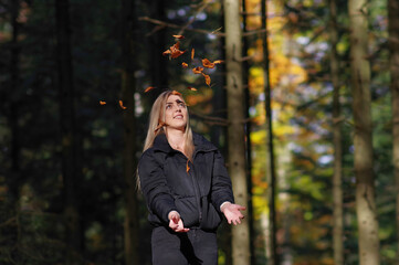 Dziewczyna blond podrzucająca liście w lesie, jesienią.