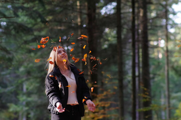 Kobieta podrzucająca liście jesienne w lesie.
