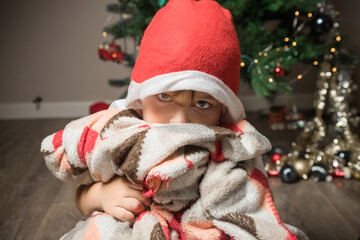 A little boy dresses up an artificial Christmas tree.  Preparation for Christmas and New Year. Santa's red hat.