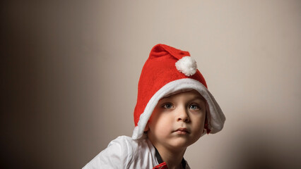 A little boy dresses up an artificial Christmas tree.  Preparation for Christmas and New Year. Santa's red hat.