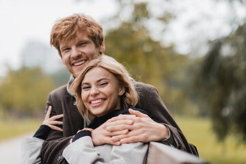 cheerful young man hugging positive woman in green park.