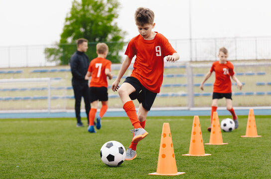 Training football session for children on soccer camp. Boy in children's soccer team on training. Kids practicing outdoor with a soccer balls. Young boy improving dribbling skills. Training with cones
