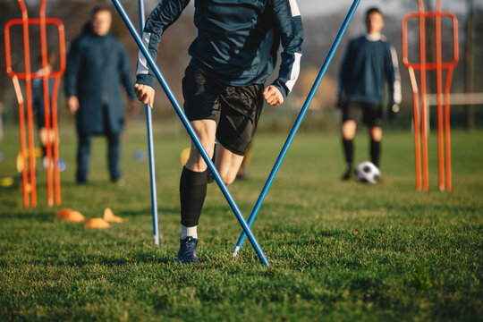 Young Football Players Running Slalom And Jumping Over Poles. Soccer Practice For Teenage Boys. Junior Level Soccer Team Traing Unit