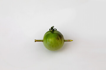 A green tomato with a nail sticking thru it