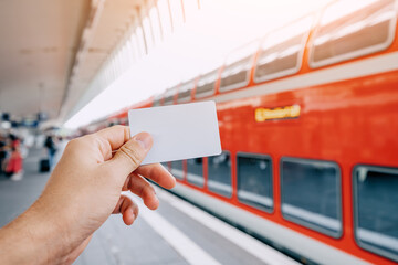 Credit or prepaid transport card in the passenger's hand against the background of a modern double-decker high-speed train on the platform of the railway station