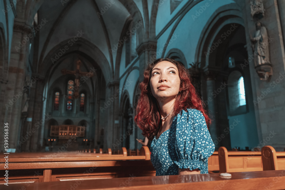 Wall mural the girl prays in the catholic church and asks god for health, forgiveness of sins and finding spiri