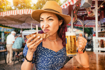 A girl in a pub sniffs a spoiled currywurst sausage and makes a disgruntled face while holding a beer in her other hand