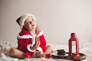 Cute child girl 3-4 year old wear red santa claus hat and bathrobe sit in bed with Christmas decor...
