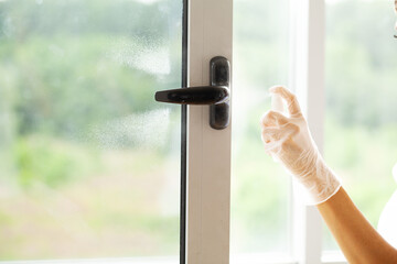Woman cleaning window, window knob with alcohol spray at the house.