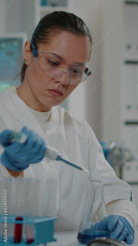 Poster vertical video: lab worker using micro pipette with beaker and test tubes to do substance experiment