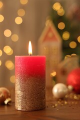 Beautiful burning candles with Christmas decor on wooden table against blurred festive lights