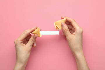 Woman holding tasty fortune cookie and paper with prediction on pink background, top view. Space...
