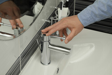Man using water tap in bathroom, closeup