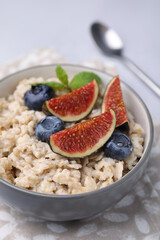 Oatmeal served with blueberries, mint and fig pieces on light grey table, closeup