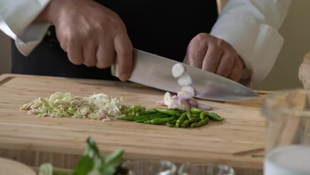 Slicing Shallot, red onion on a wooden cutting board into slice pieces with a kitchen knife by professional chef.
