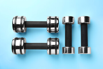 Many stylish dumbbells on light blue background, flat lay