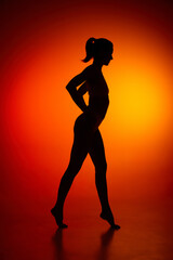 Fototapeta na wymiar Silhouette of female full-length body isolated over orange background. Side view.